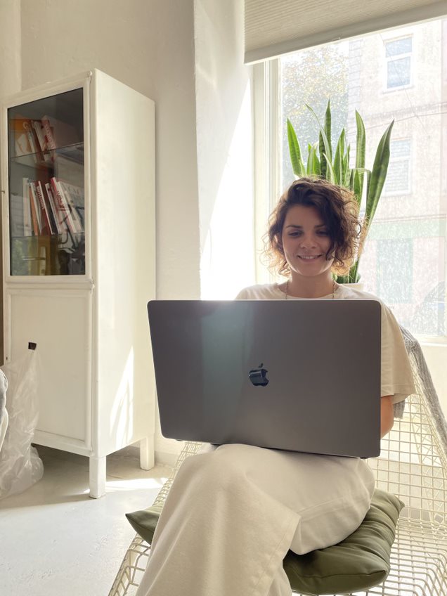 Person sitzt auf einem Stuhl mit refurbished MacBook auf dem Schoß