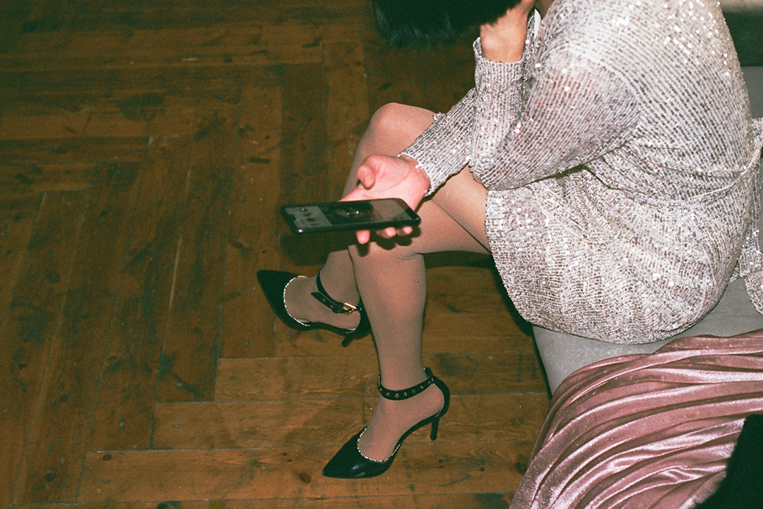 woman in a party dress sitting on the couch and scrolling through her phone
